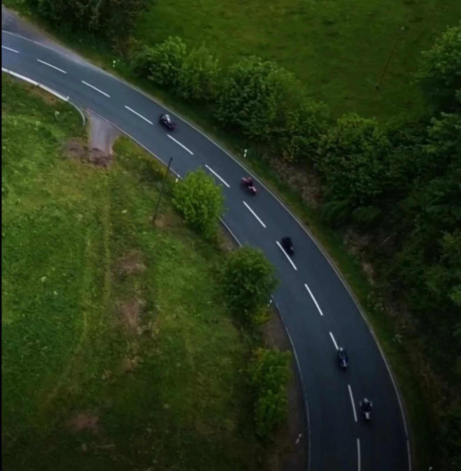 Dronebeeld van motoren in een lange bocht door het groen